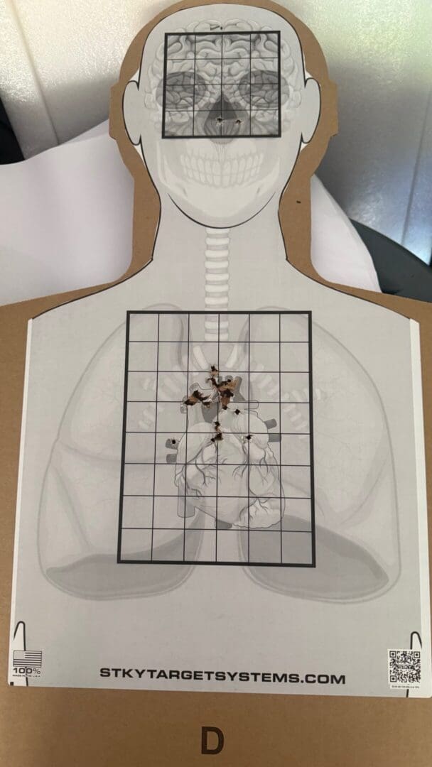 Paper shooting target with clustered bullet holes in the center mass.