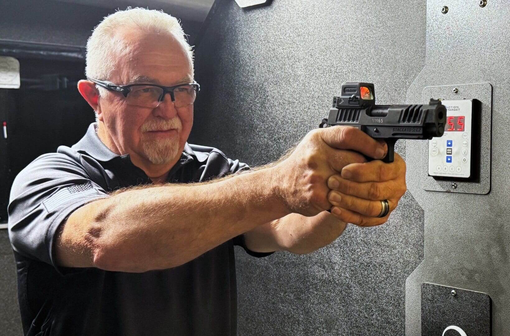 Elderly man aiming a handgun at a shooting range.