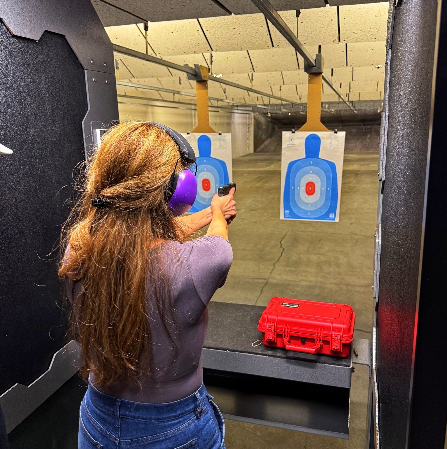 Person aiming at a blue paper target in an indoor shooting range.