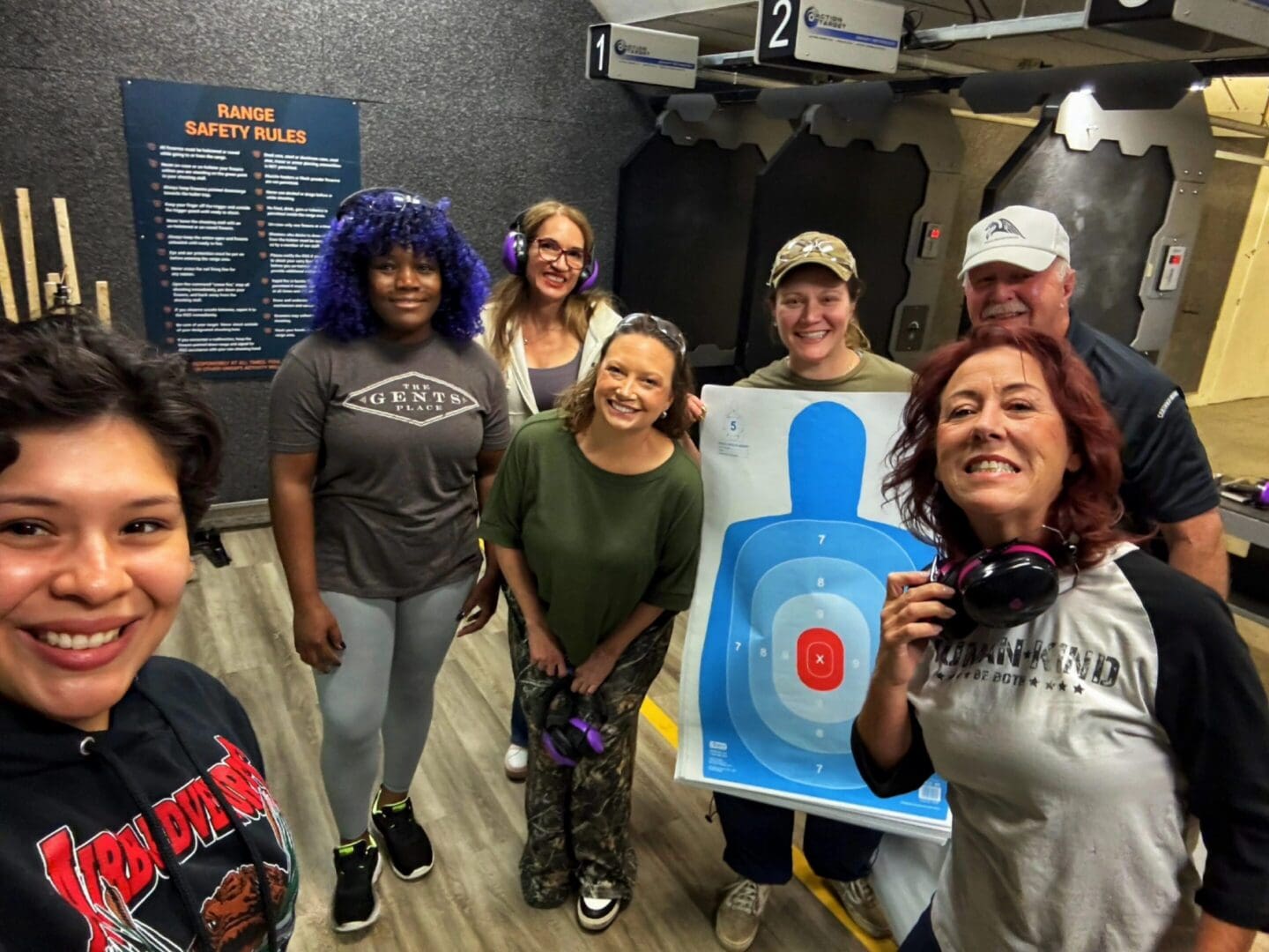 Group of six people smiling indoors with a shooting target.