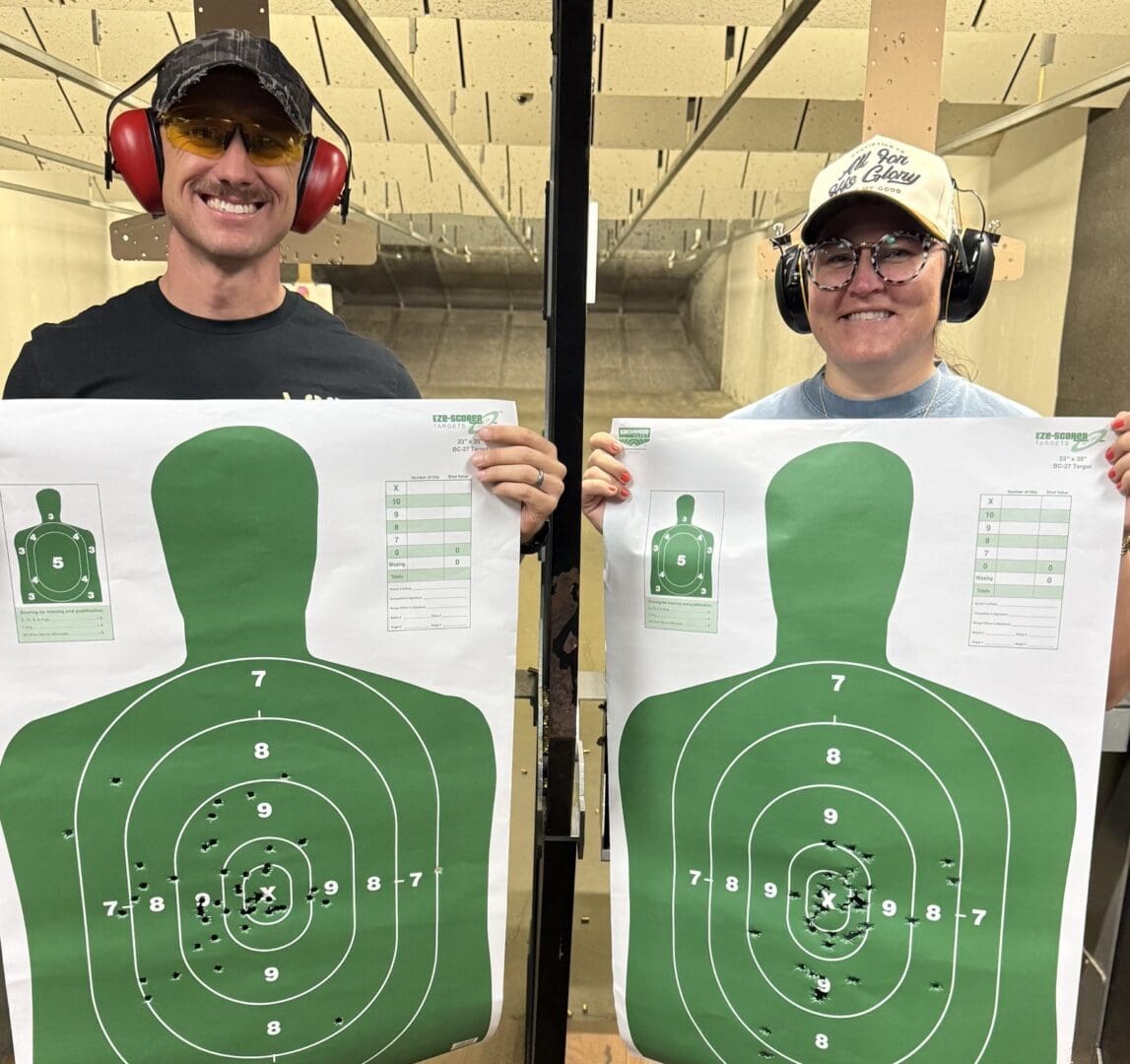 Two shooters holding bullet-pierced silhouette targets